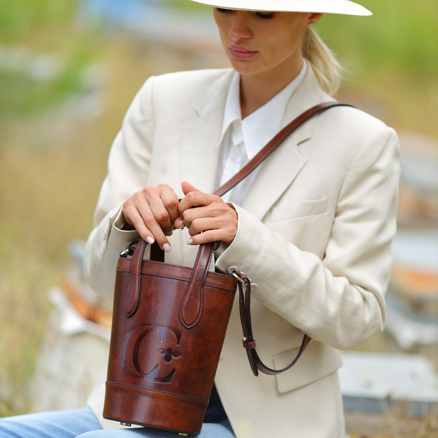 Forever Alice bucket bag in cognac leather by Cecily Clune being held with two hands on lap